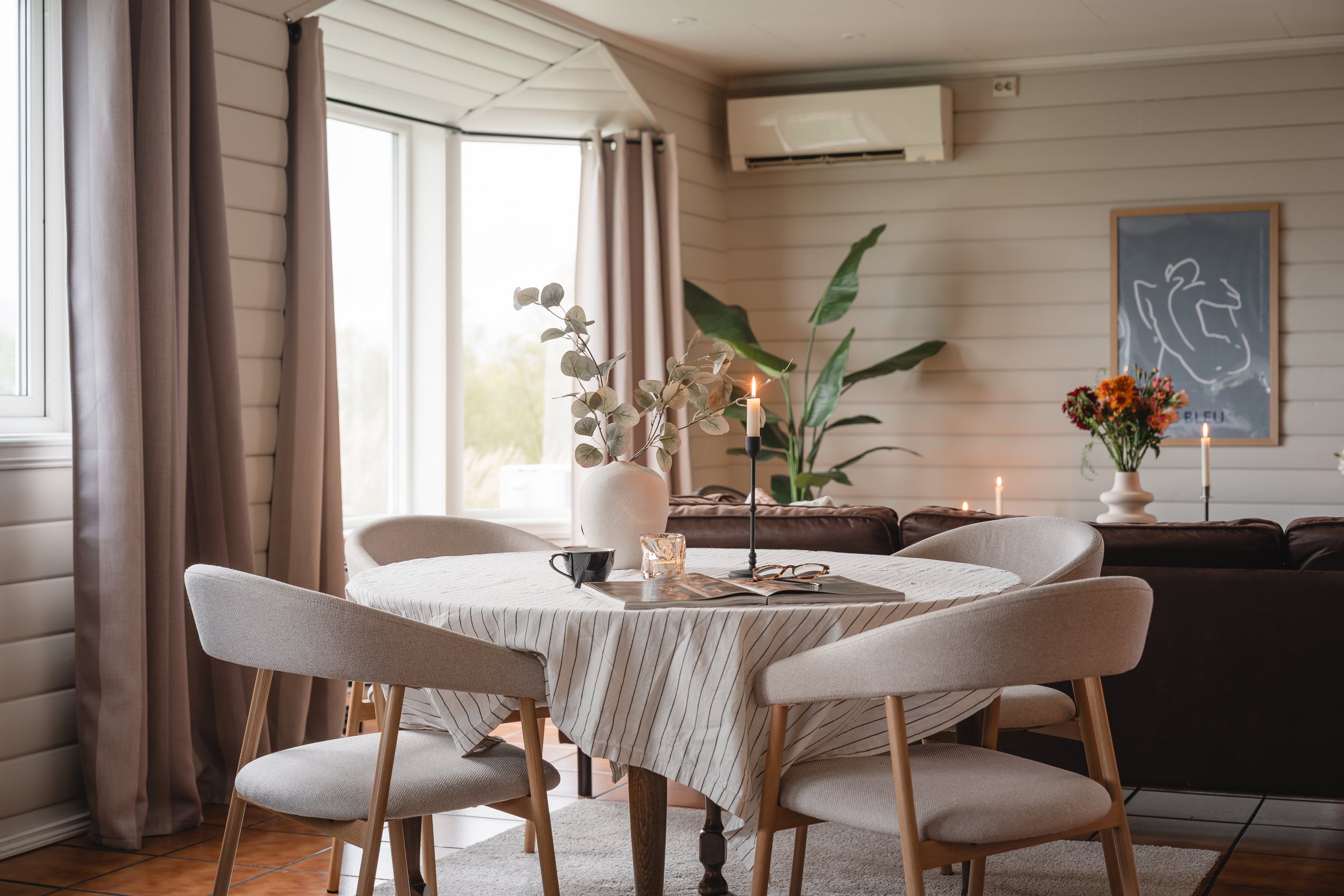 Dekket spisebord med lyse stoler foran store vinduer