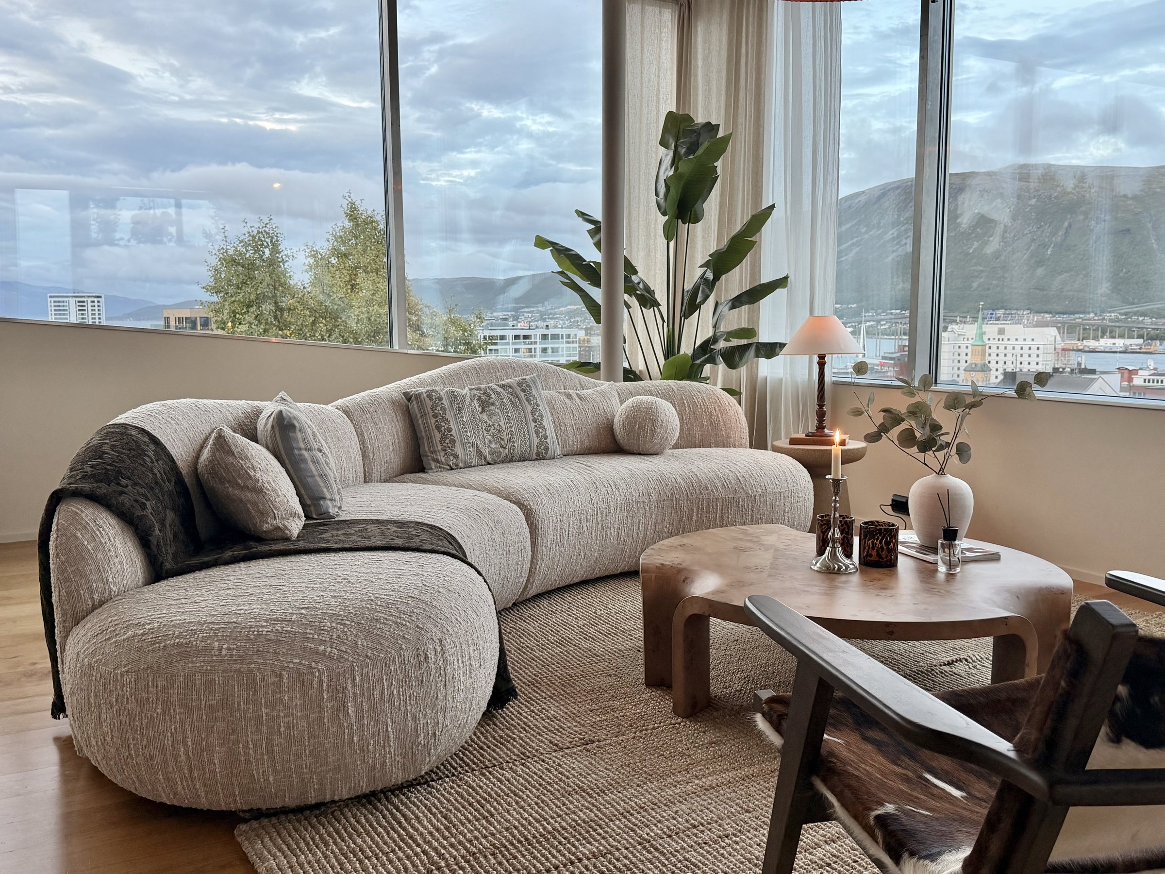 Stue med buet bouclésofa, sofabord i tre og stor vindusflate